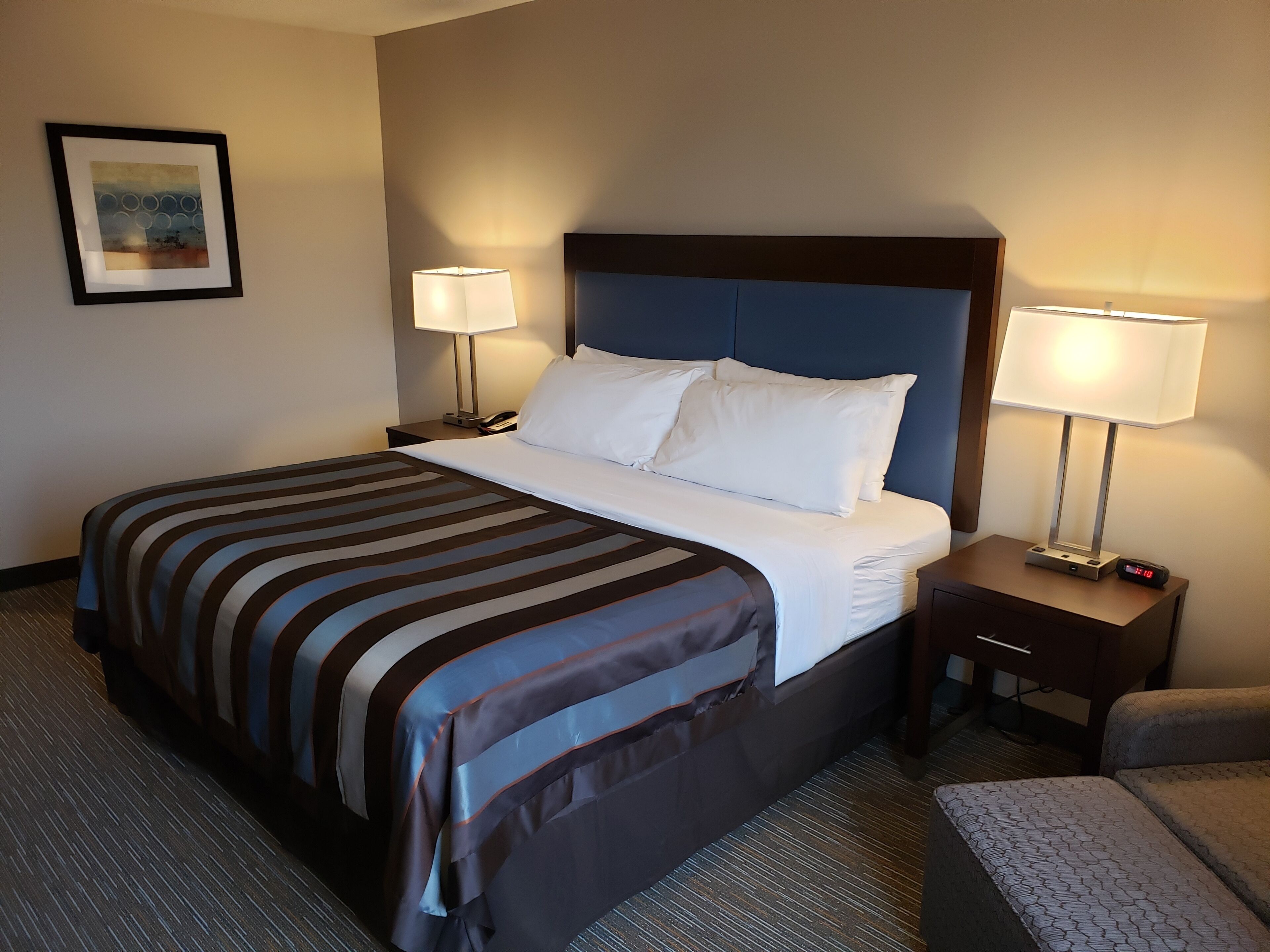 A hotel room with a large bed, two bedside tables with lamps, a framed picture on the wall, and a small chair.
