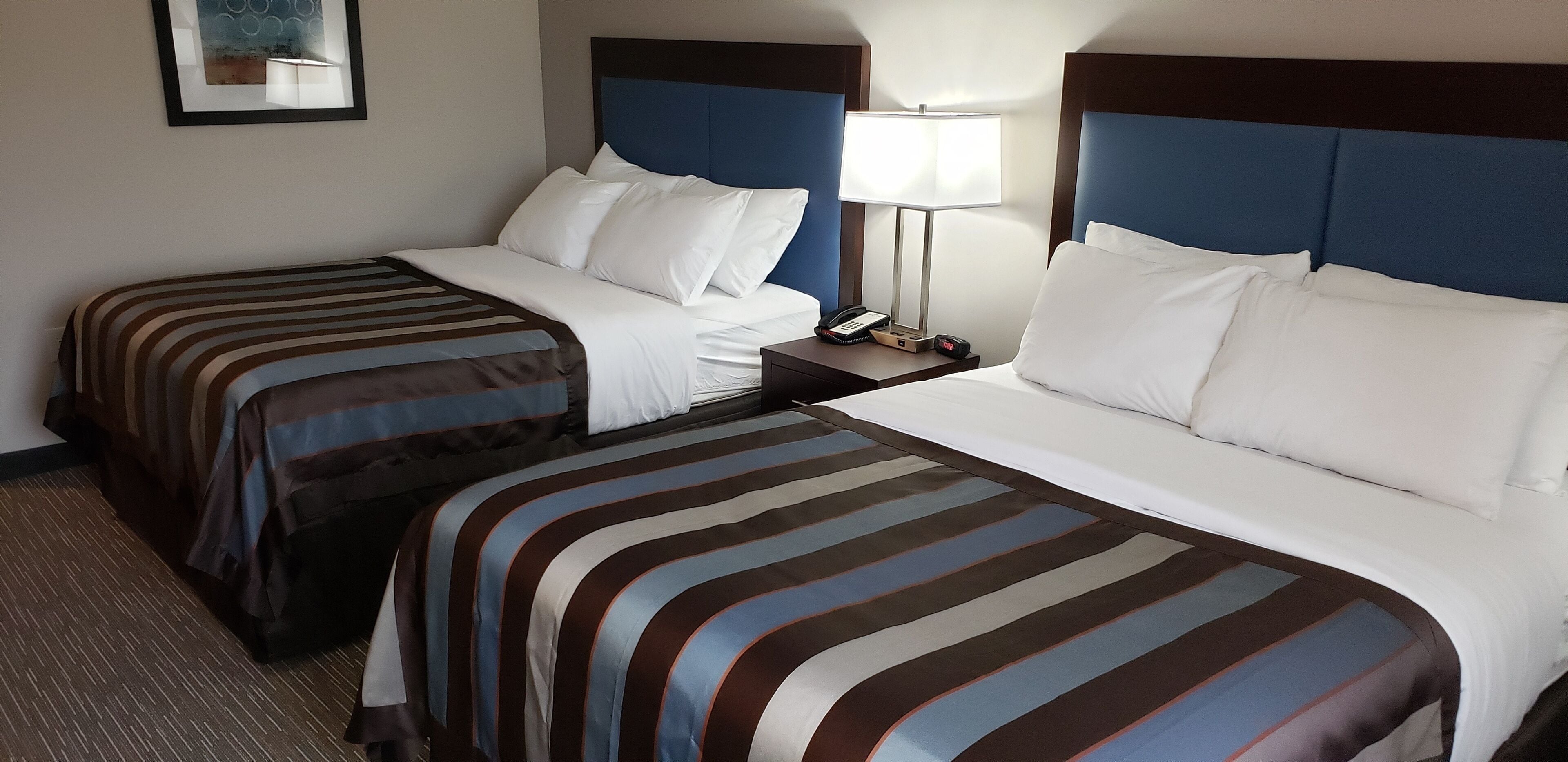 Ein Hotelzimmer mit zwei Betten, jeweils mit gestreifter Bettwäsche und weißen Kissen. Ein Nachttisch mit Lampe und Telefon ist ebenfalls vorhanden.