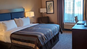Una habitación de hotel con una cama grande, un escritorio, una silla, una lámpara y una ventana con cortinas.
