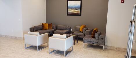 Un área de espera moderna con sofás grises y sillones blancos, una mesita y un cuadro en la pared.