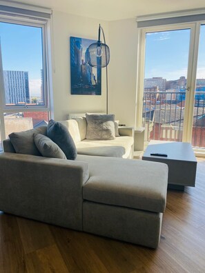 Relax in this stylish living room with a large L-shaped sofa, side table, and floor lamp, offering a view of the city outside through large windows.