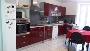 Une cuisine moderne avec des meubles rouges, un lave-vaisselle blanc et un coin repas comprenant une table et des chaises rouges.