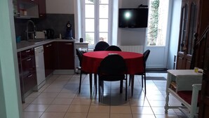 Une cuisine compacte avec un coin repas, un téléviseur fixé au mur et une vue sur l’extérieur par une fenêtre.
