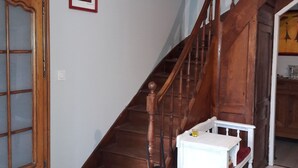 Un escalier avec des rampes en bois, une table blanche avec un coussin rouge et un meuble en bois doté de portes en verre.
