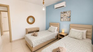 A hotel room with two beds, a wall-mounted air conditioner, a bedside lamp, and a decorative number board. - Narcissos 'Nissi Beach' Apartment D9 (Ayia Napa)