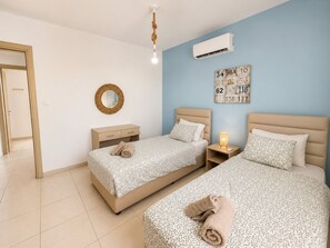 A hotel room with two beds, a wall-mounted air conditioner, a bedside lamp, and a decorative number board. - Narcissos 'Nissi Beach' Apartment D9 (Ayia Napa)
