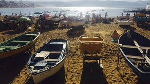 Een strand met verschillende boten die op het zand liggen, een heldere lucht en een vergezicht op zee en bergen.