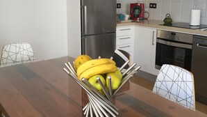 Een moderne keuken met witte kasten, roestvrijstalen apparatuur en een houten eettafel met een fruitschaal.