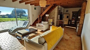 A spacious living area with a sofa, armchairs, and a coffee table. A staircase leads to an upper level, and a large window offers a view of the outdoors.