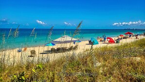Una playa con agua turquesa cristalina, orilla arenosa y varias sombrillas de playa.