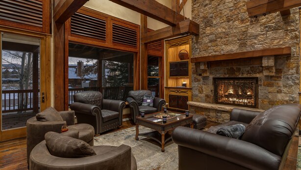 A cozy living room with leather furniture, a stone fireplace, and large windows overlooking a snowy landscape. - Mega 10,000 sq.ft. Home w/ Hot Tub + Ski Shuttle - Rocking Chair Lodge (Steamboat Springs)