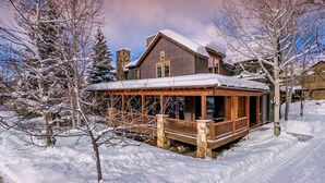 A snow-covered lodge with a wooden porch and stone chimney. - Mega 10,000 sq.ft. Home w/ Hot Tub + Ski Shuttle - Rocking Chair Lodge (Steamboat Springs)