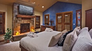 A bedroom with a stone fireplace, a bed with multiple pillows, and wooden shutters on the windows. - Mega 10,000 sq.ft. Home w/ Hot Tub + Ski Shuttle - Rocking Chair Lodge (Steamboat Springs)