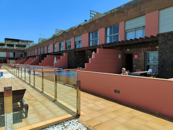 A modern building with a swimming pool, outdoor seating, and a clear sky.