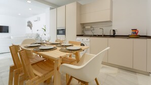 Una cocina moderna con comedor, mesa de madera, sillas blancas y horno empotrado.