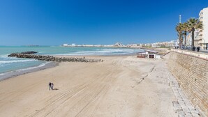 Una playa con un muro de piedra, un edificio pequeño y palmeras.
