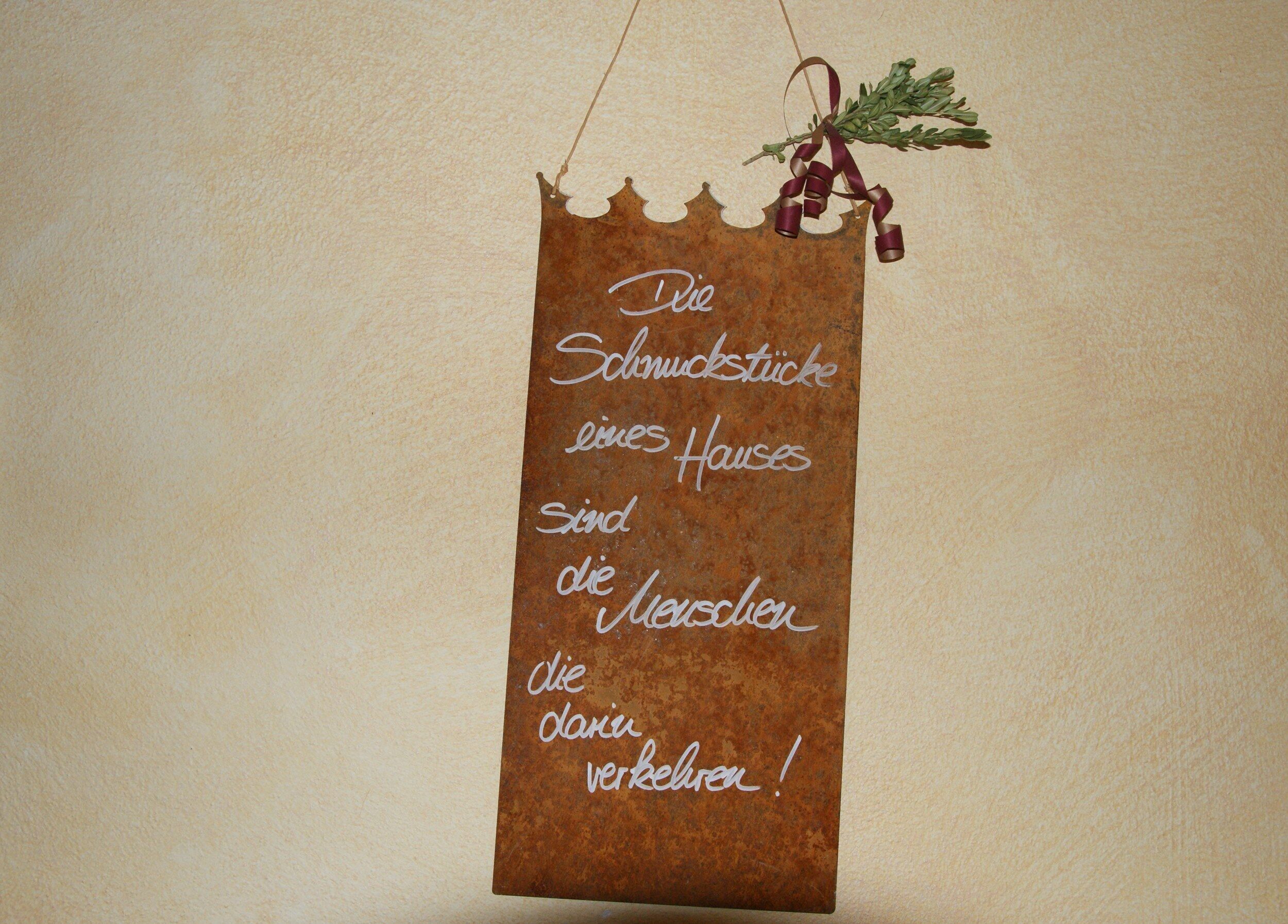A hanging sign with a rustic design, featuring a message in German.