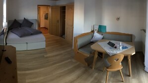 A compact hotel room with a bed, a small sofa, a table with a chair, and a wardrobe.