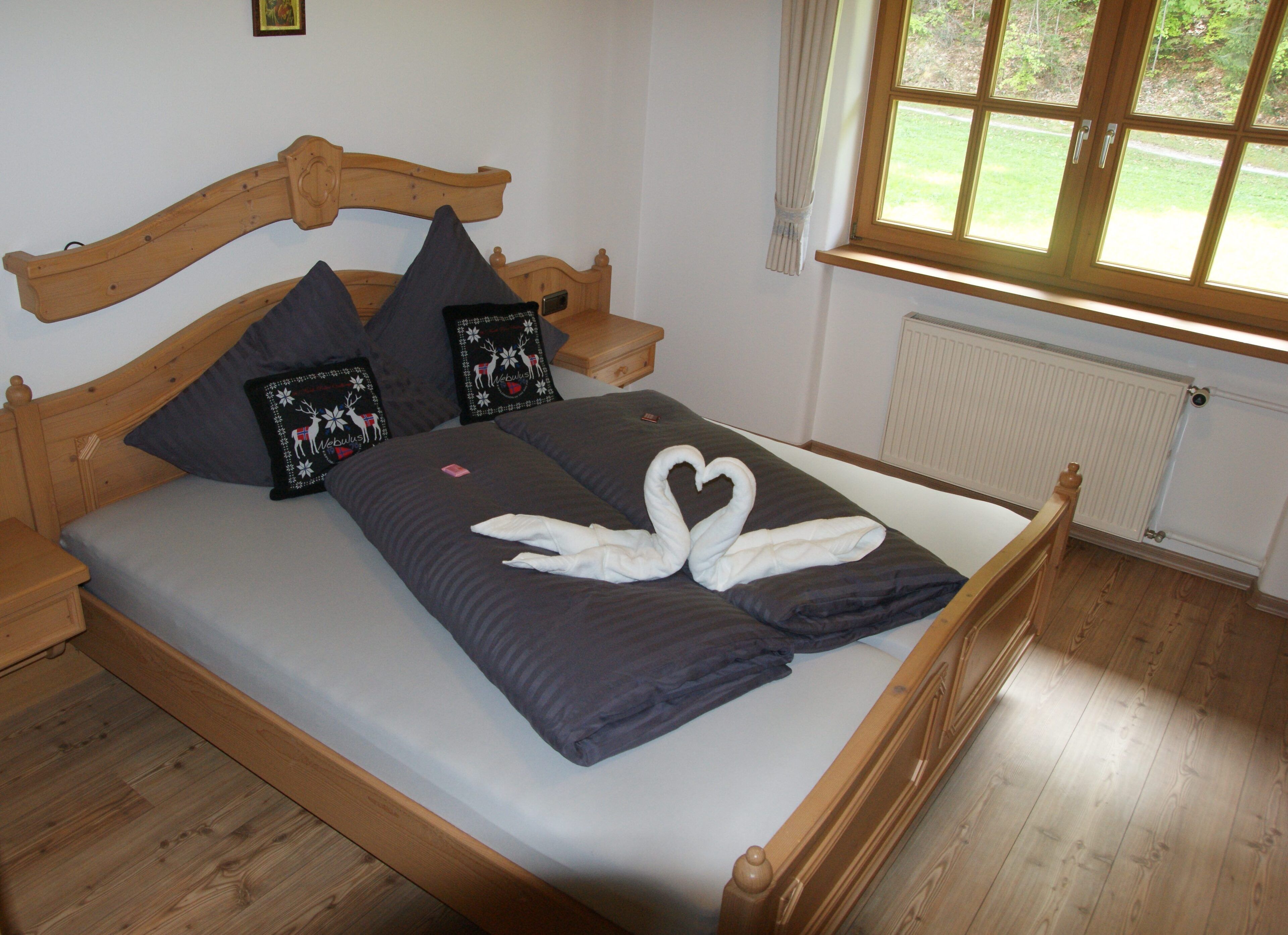 A wooden bed with grey bedding, two decorative pillows, and a swan-shaped towel arrangement.