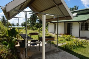 Un espace extérieur abrité, équipé d’une table et de chaises, d’un barbecue, et une maison avec un toit végétalisé en arrière-plan.