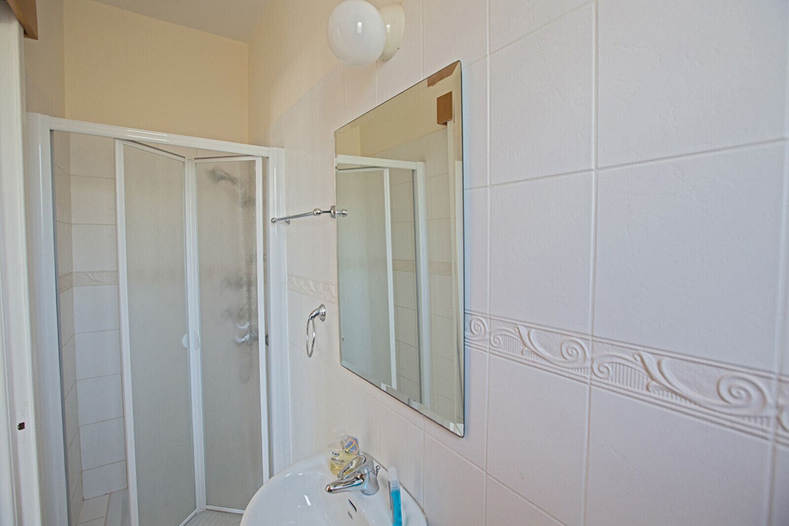 A bathroom with a shower, a sink, a mirror, and a light fixture.