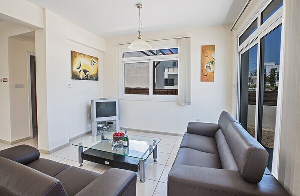 A modern living room with a sofa, a glass coffee table, a television, and artwork on the walls.