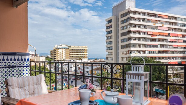 Ein Balkon mit einem Tisch, der für Tee gedeckt ist, mit Blick auf eine Skyline aus modernen Gebäuden und einem wolkenlosen Himmel.