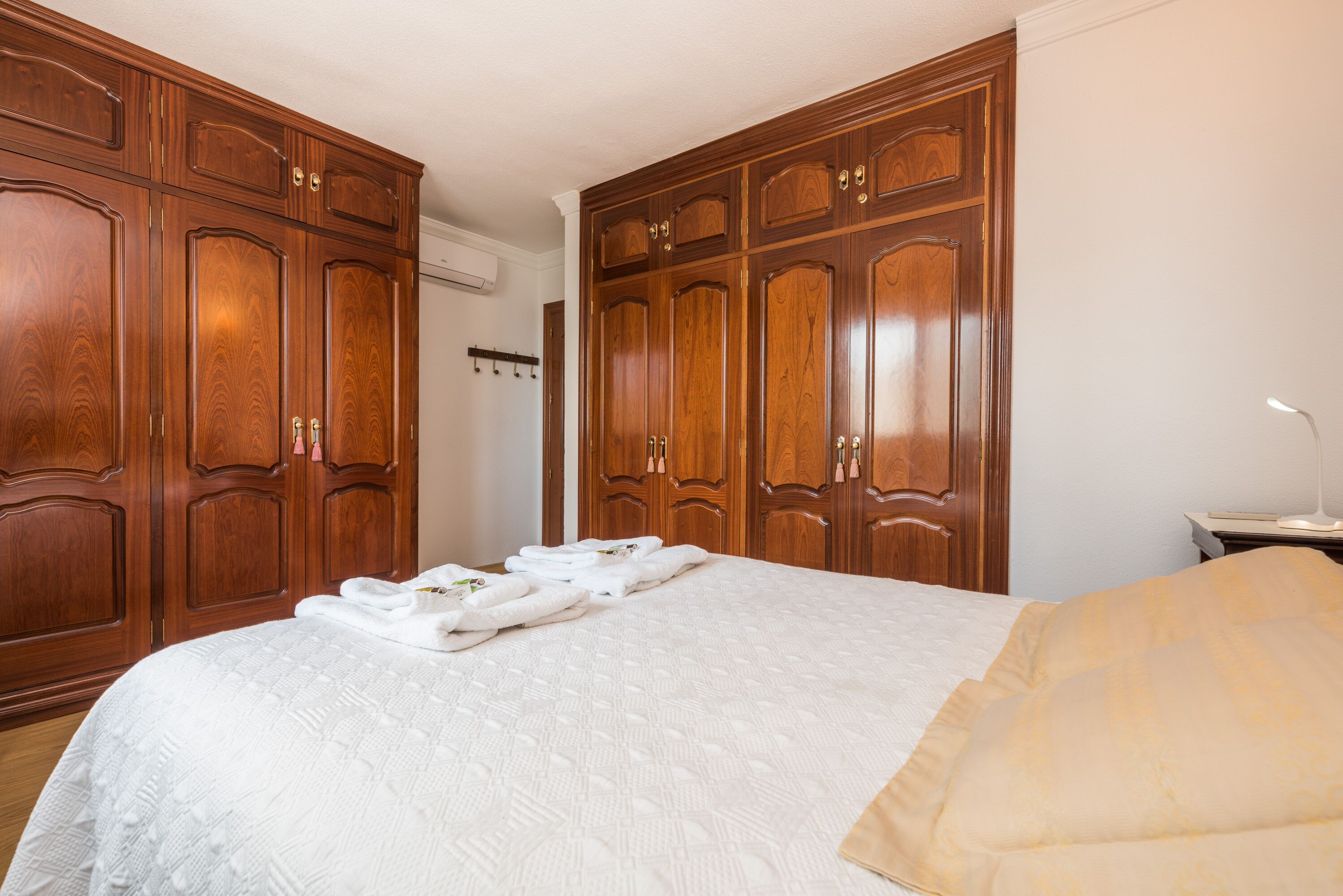 A hotel room with a large bed, wooden wardrobes, and a small bedside table.