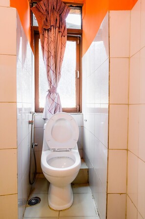 A small, compact bathroom with a toilet, a window with curtains, and tiled walls. - Hotel Pomelo House (Kathmandu)