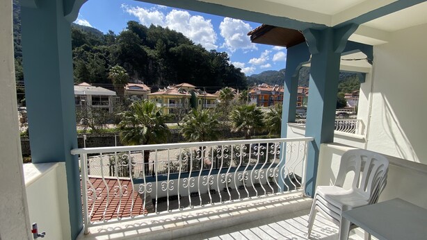 Un balcon donnant sur un quartier résidentiel, une chaise blanche et un sol carrelé.