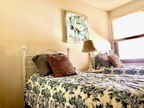 A bedroom with a bed, pillows, a lamp, and a painting on the wall.