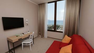 Ein Hotelzimmer mit Fernseher, Schreibtisch, Stuhl und einem roten Sofa mit orangefarbenen Kissen.