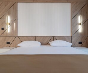 A modern bedroom with a wooden headboard, two bedside lamps, and a large window with blinds. - Hotel Tara (Bečići)