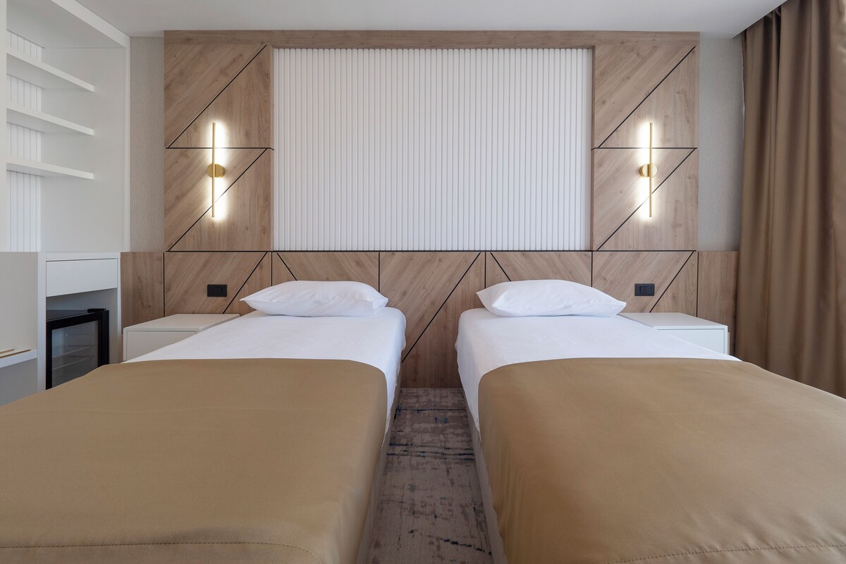 A hotel room with two beds, a wooden headboard, and wall-mounted lights.