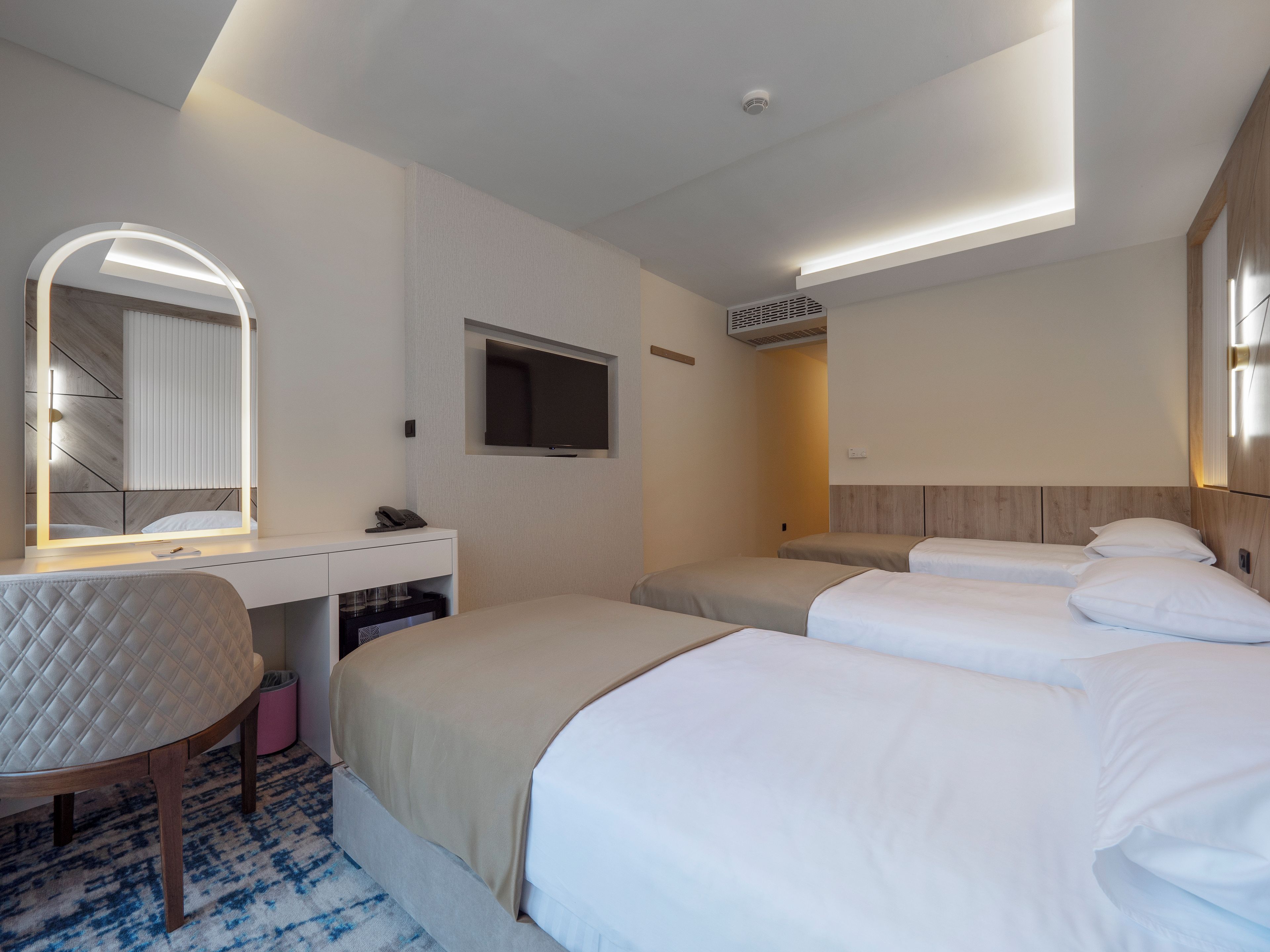 Une chambre d’hôtel comprenant un lit, un bureau avec un miroir, une télévision et un luminaire au plafond.