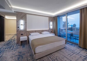 A modern hotel room with a large bed, a bedside table, a nightstand, a large window with a view, and a ceiling with recessed lighting. - Hotel Tara (Bečići)