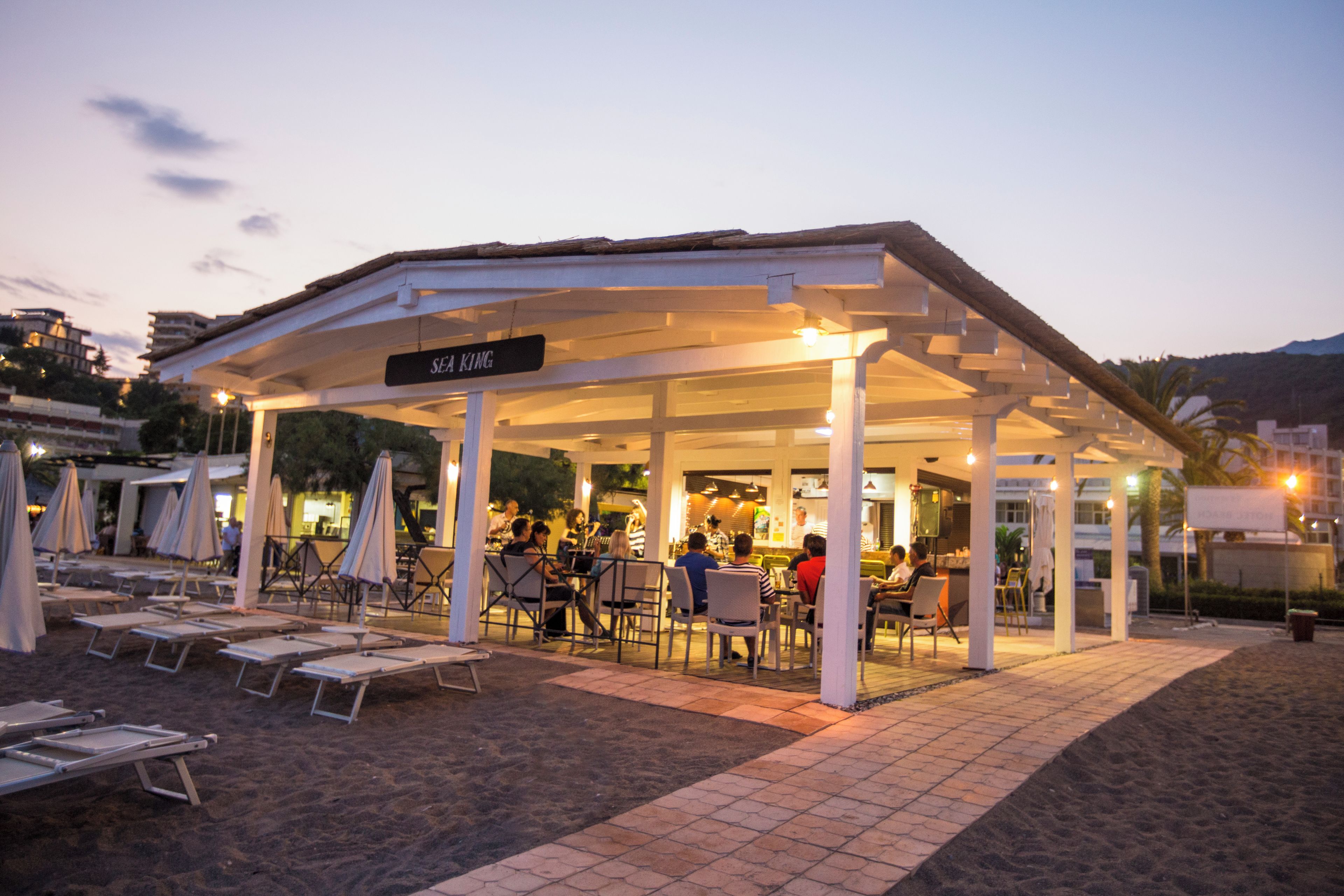 A beachside restaurant with outdoor seating, a covered area, and a sign indicating the name.
