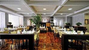 A spacious dining area with multiple tables and chairs, a central plant, and a modern ceiling design. - Hotel Tara (Bečići)
