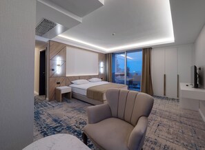 Una habitación de hotel moderna con cama, una silla, un escritorio, televisor y un gran ventanal con vistas.