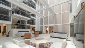 Un amplio atrio de varios niveles con mobiliario moderno, una escalera y un gran muro de cristal.