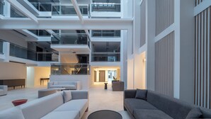Un interior espacioso con techo alto, una zona de estar central con sofás y una mesa de centro, y una escalera que conduce a niveles superiores.