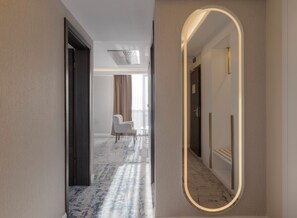 Un pasillo de hotel con piso de mármol, un espejo grande, una puerta y una silla a lo lejos.