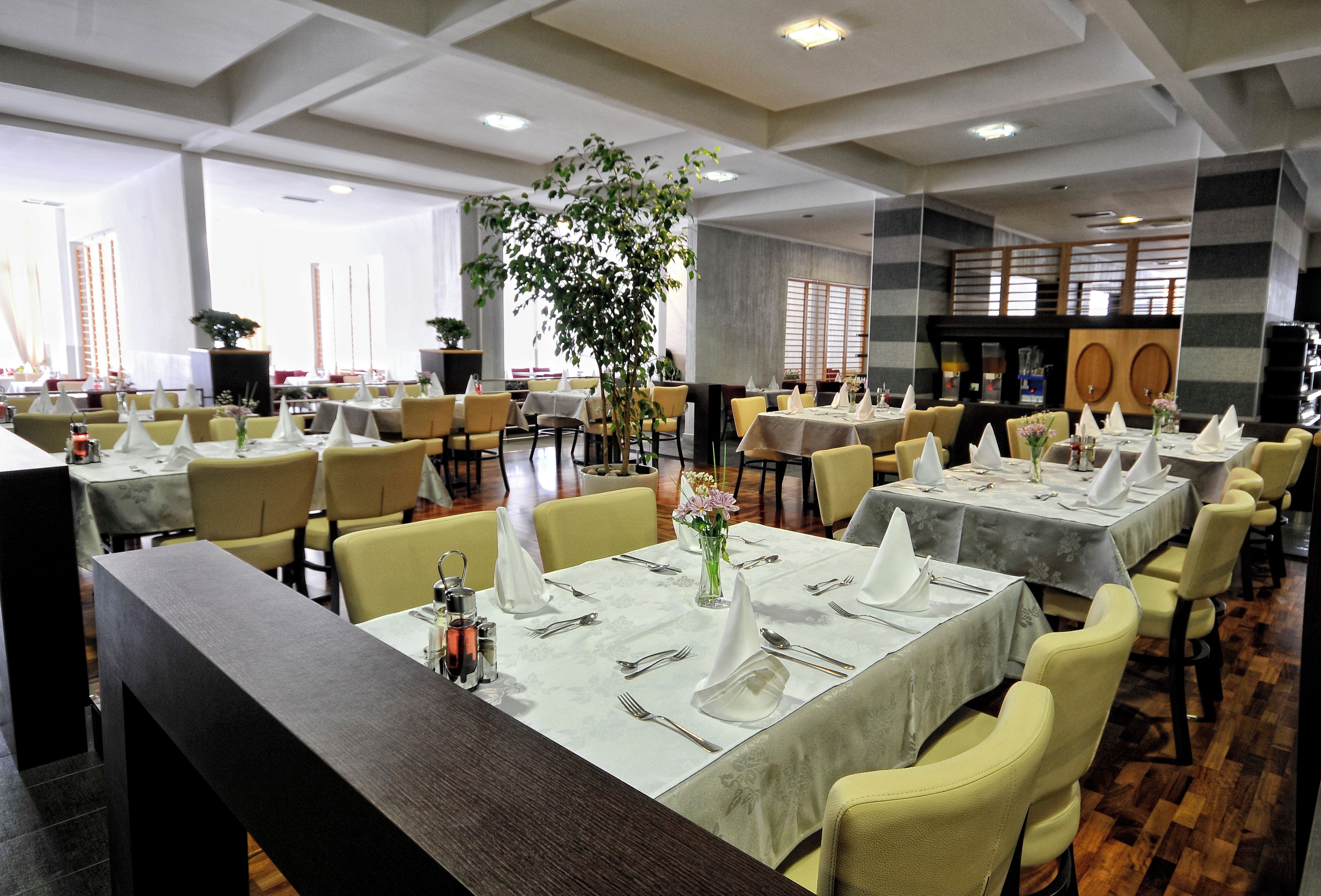 A restaurant with multiple tables set for dining, chairs, and a large potted plant.