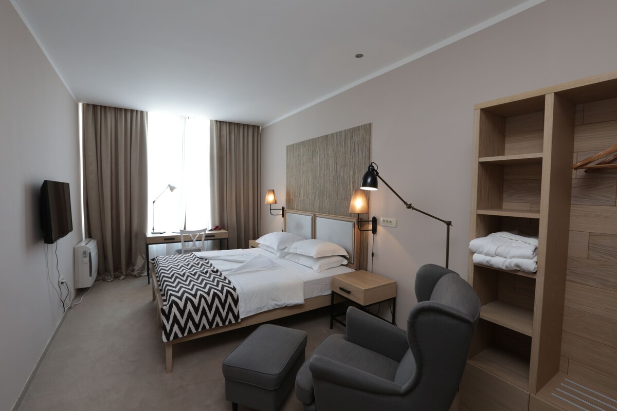 A hotel room with a bed, bedside tables, a desk, a chair, a wardrobe, and a flat-screen TV.