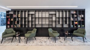 Un interior moderno con cuatro sillones verdes, una estantería negra y una alfombra estampada.
