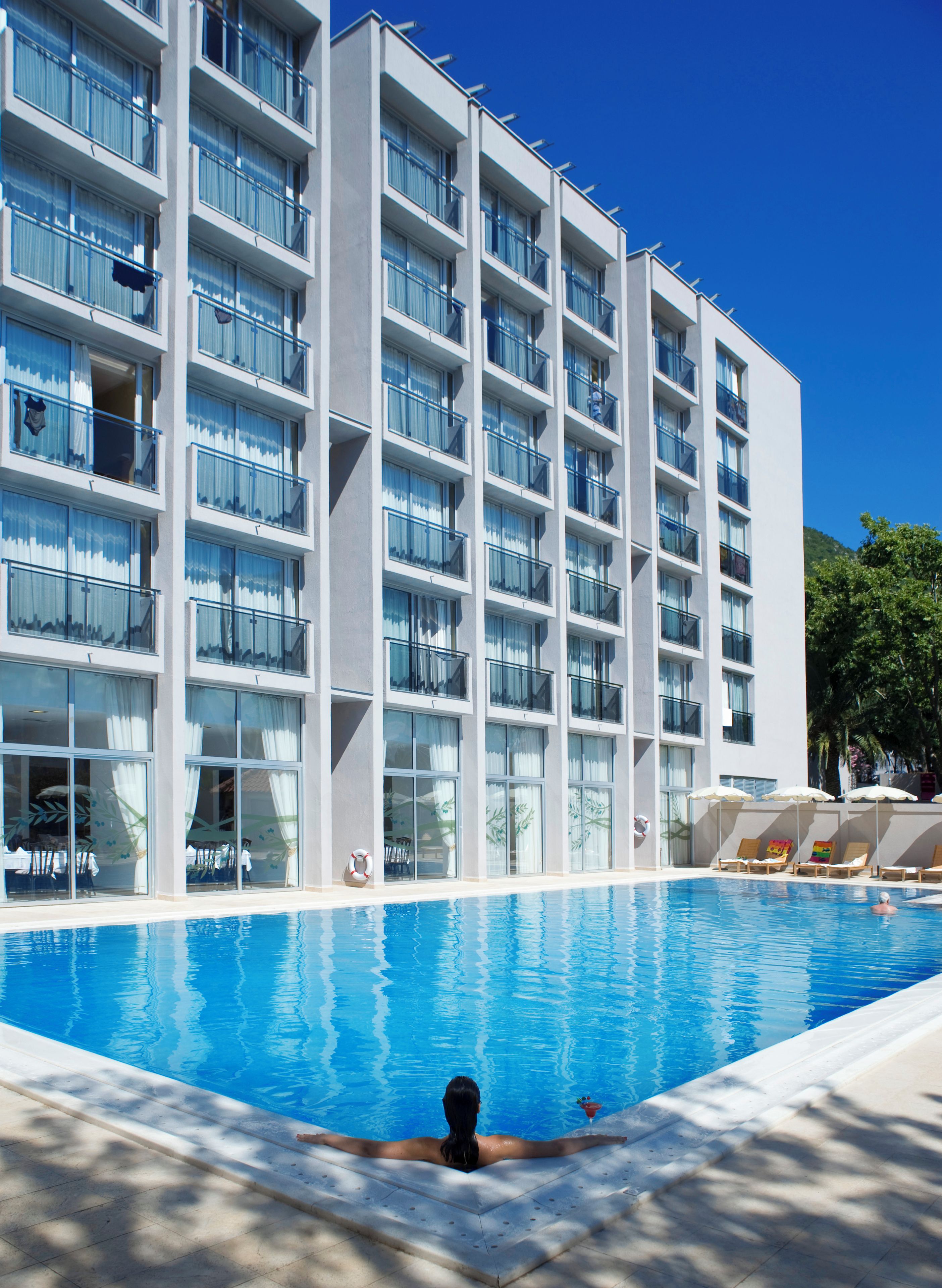 Ein modernes Hotel mit Schwimmbad, mehreren Balkonen und Liegestühlen.
