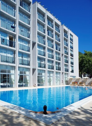 Un hotel moderno con piscina, varios balcones y tumbonas.