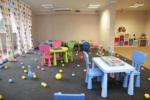A children's playroom with colorful furniture, a table with a board game, and scattered toys. - Hotel Tara (Bečići)