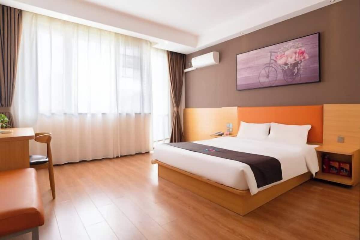 A hotel room with a bed, a desk, a chair, and a window with curtains.