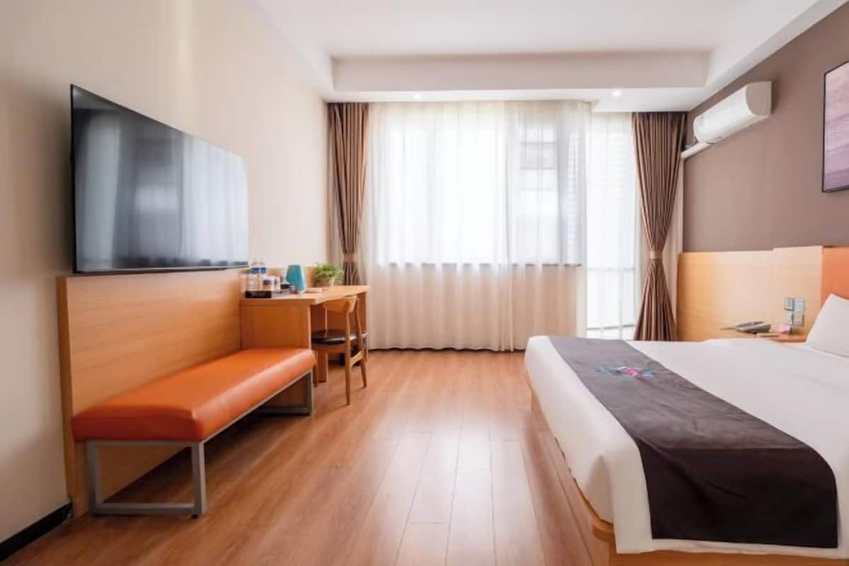 A hotel room with a bed, a desk, a chair, a bench, a TV, and a window with curtains.